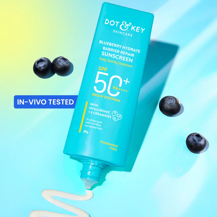 Turquoise sunscreen tube with white lotion, three blueberries, and a blue background.