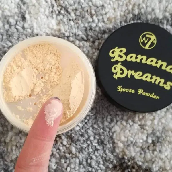 Open container of loose banana powder with lid and a finger dipped in the powder.