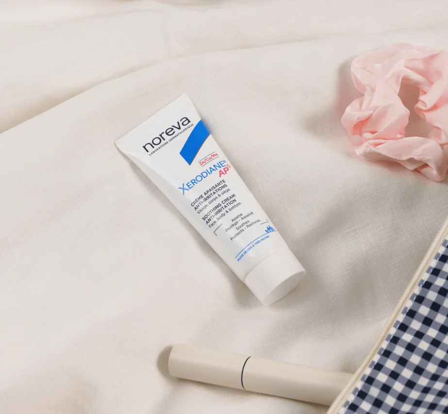 White tube of La Roche-Posay cream on a soft cream-colored fabric with accessories nearby.