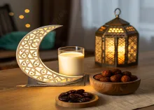 Lit crescent moon decor, lantern, glass of milk, and bowls of dates on a wooden table.