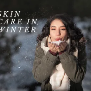Woman in winter coat blowing snow from her hands outdoors.