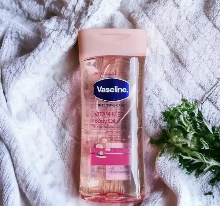Vaseline lotion bottle on a white textured cloth next to green leafy sprigs.
