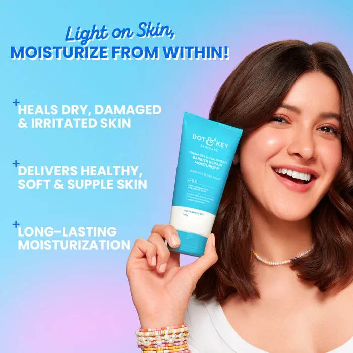 Smiling woman holding a blue skincare product tube against a pastel background.