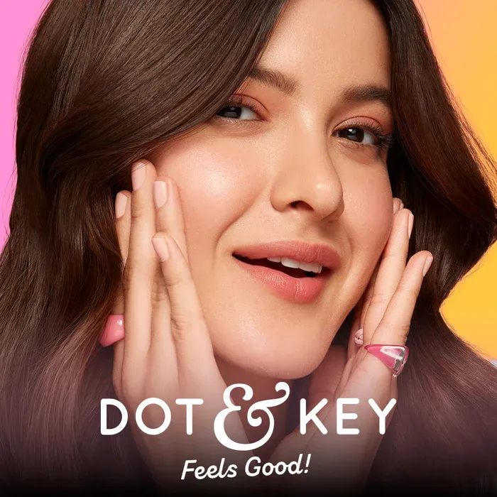 Woman with flawless skin smiling, hands on cheeks, Dot & Key logo at the bottom.