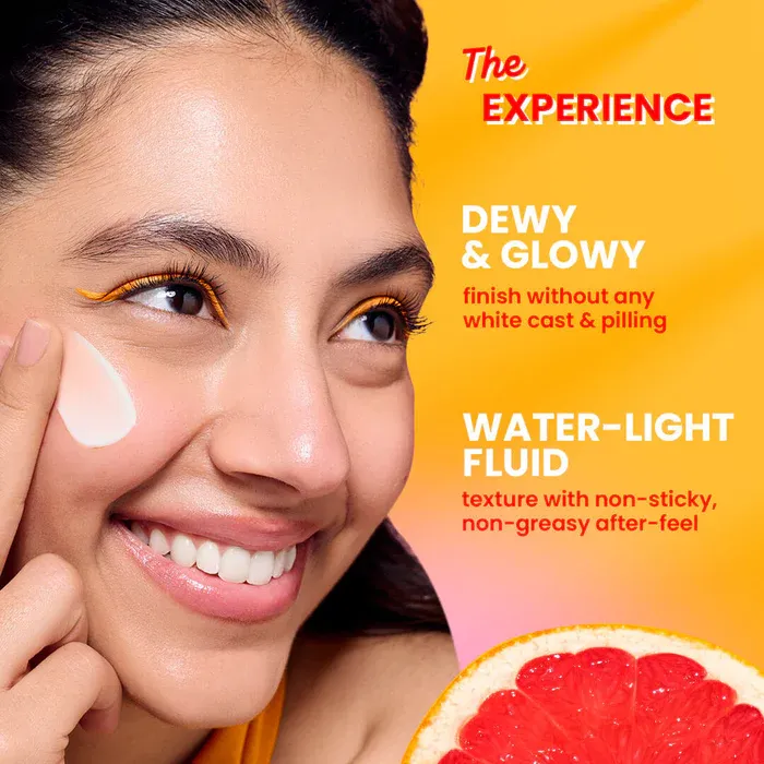 Smiling woman applying cream to her cheek with a grapefruit in the corner on a yellow background.