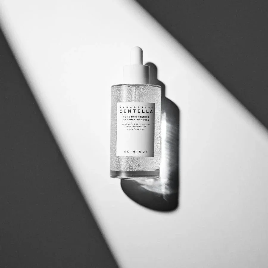 Clear serum dropper bottle illuminated by diagonal light on a gray and white surface.