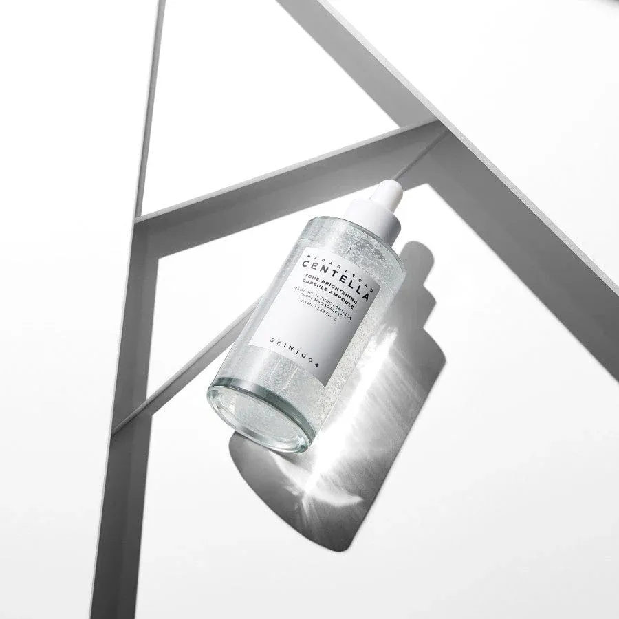 Clear serum bottle casting a shadow on a white geometric surface.