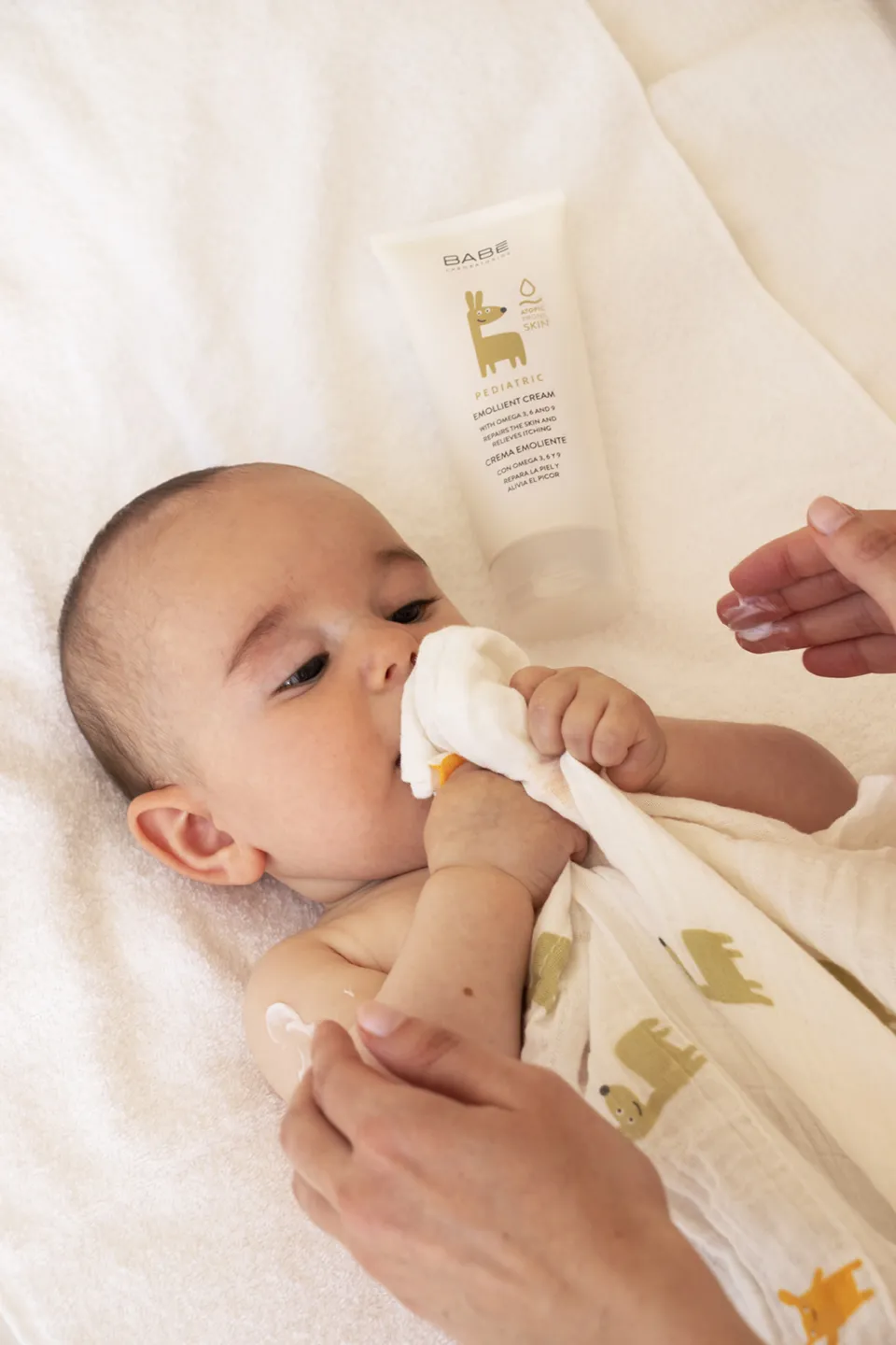 Adult gently wiping a baby’s nose with a soft cloth on a white blanket.