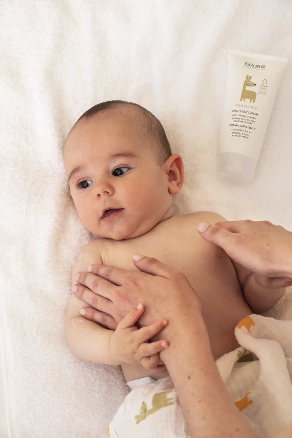 Baby lying on a white blanket with an adult gently massaging their chest.