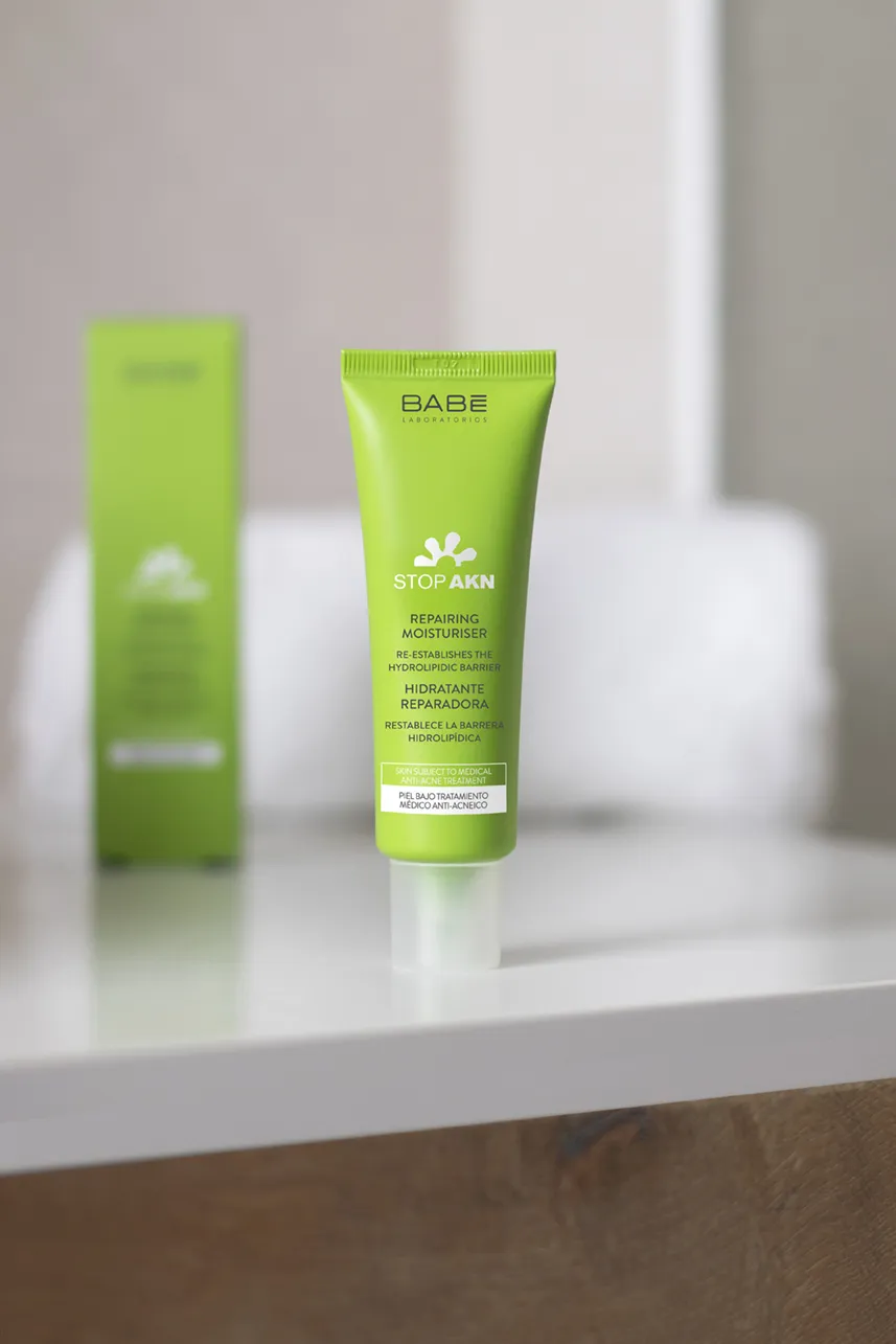 Green skincare tube and box on a white bathroom counter with blurred background.