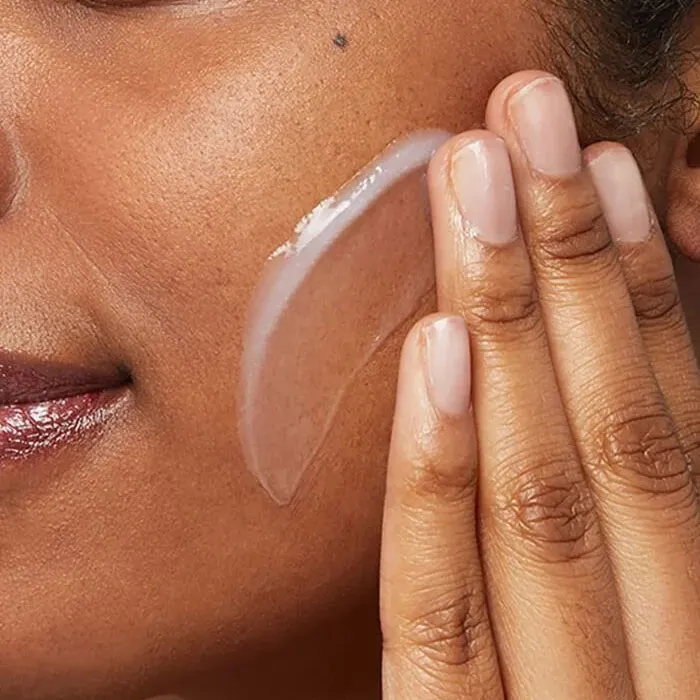Fingers applying clear gel moisturizer to a woman's cheek.