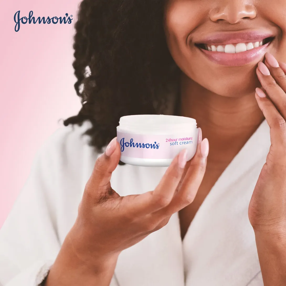 Smiling woman holding Johnson's cream jar against a soft pink background.
