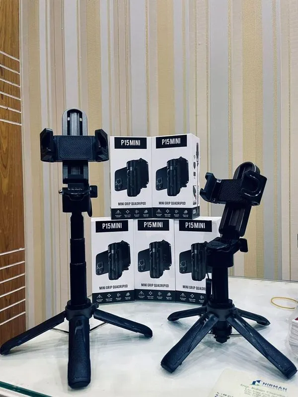 Two black phone tripod stands on a table with product boxes in the background.