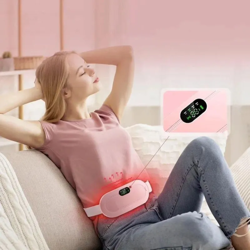 Woman relaxing on a couch using a pink heating pad belt on her abdomen.