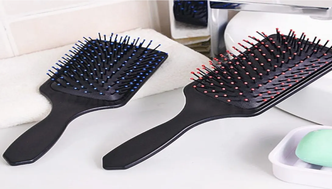 Black paddle hairbrushes with colored bristles on a bathroom counter.