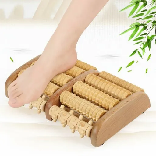 Bare foot using a wooden roller foot massager on a white surface with green leaves nearby.