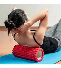 Woman using a red textured foam roller on her upper back while lying on a yoga mat.
