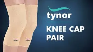 Beige knee cap supports worn on both legs with Tynor logo, on a dark blue background.